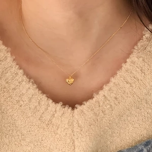 Elegant gold heart pendant necklace with tiny diamond on model wearing beige sweater