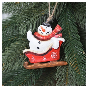 Detail of resin snowman on a red sleigh ornament hanging on a green Christmas tree