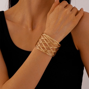 Detail view of a gold-plated woven mesh cuff bracelet on a woman wearing black clothing
