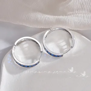 Detail shot of silver hoop earrings featuring blue rectangular gemstones on white silk