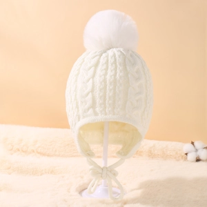 Detail of cable knit pattern and large fluffy pompom on cream baby earflap winter hat