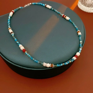 Detailed macro shot of a blue beaded necklace with red and silver accents on a jewelry box
