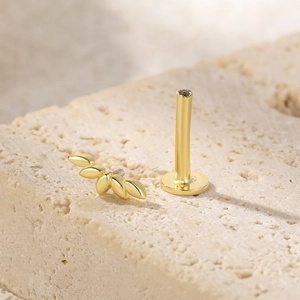 Macro view of gold S925 sterling silver leaf cluster piercing stud on a beige stone