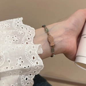 Detail eines Holzfisch-Armbands mit grünen Glasperlen am Handgelenk des Models