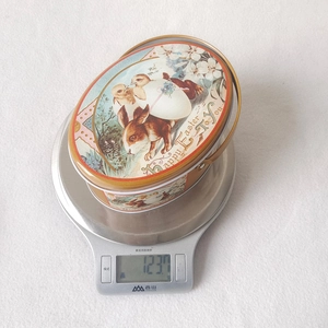 Detailed top view of Easter oval tin box weight measurement of 123.7g on scale