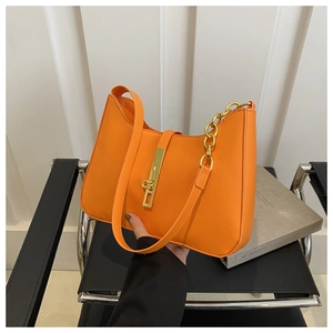 Close-up of bright orange hobo bag with gold buckle and decorative thick metal chain