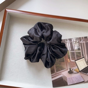 Detailed view of a black oversized silk scrunchie on a minimalist wooden tray display