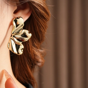 Close-up of elegant gold leaf-shaped stud earrings worn by a model to show metallic texture