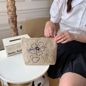 Close-up of floral embroidery on a beige canvas cosmetic bag held by a person