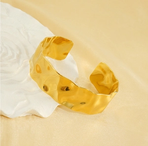Close-up of 18K gold plated wide cuff bracelet with hammered texture on a white base