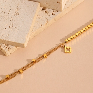 Double-layer gold clover bracelet with beaded chain on a minimalist stone display