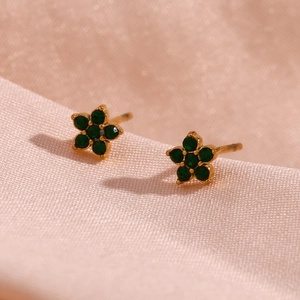 Vue macro des boucles d'oreilles fleur en or avec cristaux verts sur satin rose élégant