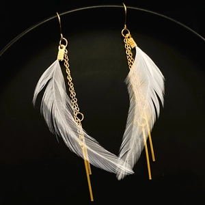 Macro detail of long white feather earrings with gold chain and metal bar accents