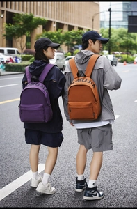 Rear view of purple and caramel nylon backpacks with MUMUJIA logo on urban street background