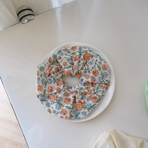 Detailed view of beige floral scrunchie with colorful petal print on a white ceramic plate
