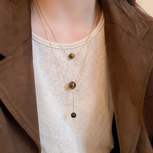Detail of layered gold-plated Y-necklace with brown tiger eye beads on a female model