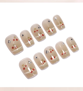 Détail d'ongles champagne œil de chat avec motifs cerises rouges et petits strass brillants