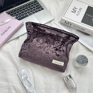 Detailed view of dark purple velvet makeup bag with soft pleated texture and woven label