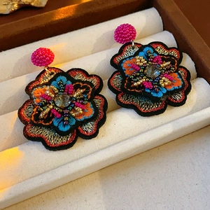 Macro detail of colorful floral beadwork embroidery earrings on a white velvet tray