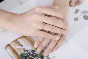 Dettaglio ravvicinato di un anello a catena d'oro con piccole perline rosa sulla mano