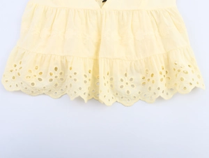 Close-up of yellow poplin fabric with broderie anglaise embroidery and ruffled hem detail
