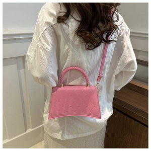 Pink quilted handbag with heart rivets and curved base shown on model in white shirt