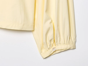 Close-up of pale yellow poplin shirt cuff featuring a translucent round button and neat stitching