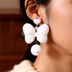 Detail of white bow pearl earrings with heart stud and plush pompom hanging elegantly