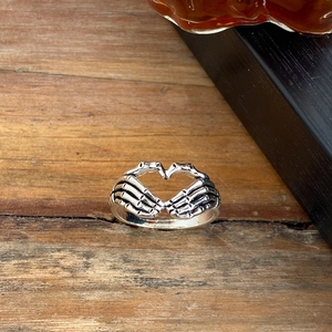 Close-up of vintage silver skeleton hands forming a hollow heart on a gothic ring