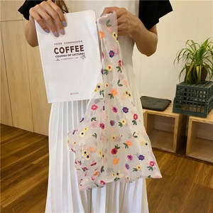 Detail of white mesh tote bag featuring colorful flower embroidery and lightweight texture