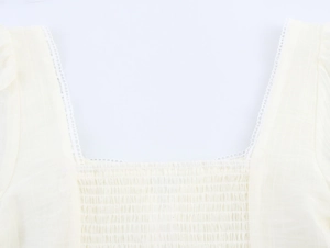 Detail of square neckline with lace trim and smocking texture on cream short blouse