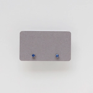 Close-up of small sapphire blue round-cut stud earrings in a six-prong silver setting