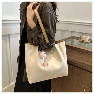 Dettaglio della borsa tote in pelle crema con tracolla marrone e ciondolo di peluche