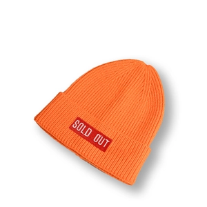 Détail du bonnet en maille orange vif montrant la texture côtelée et l'écusson SOLD OUT
