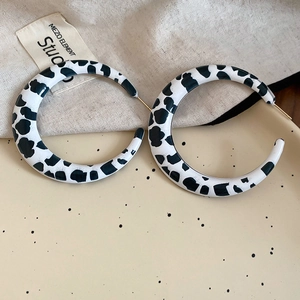 Close-up of large C-shaped hoop earrings with cow print pattern and gold studs