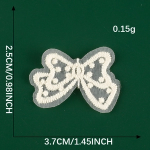 Macro detail of white lace bow patch showing dimensions 2.5cm by 3.7cm on dark background