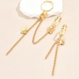 Detail of gold butterfly ring and earrings set with tassel chain on a white stone block