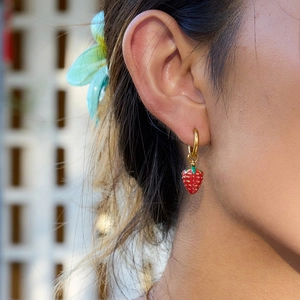 Close-up of 18K gold stainless steel hoop earrings with a red enamel strawberry pendant