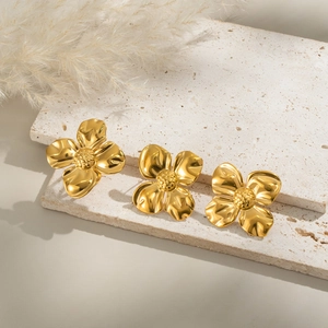 Detailansicht goldfarbener vierblättriger Blumenohrringe auf Natursteinsockel