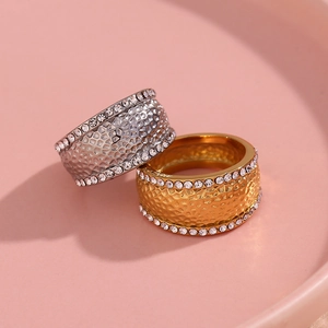 Close-up of gold and silver hammered band rings with white crystals on a pink plate