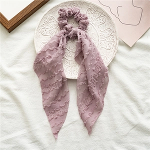 Detail of light purple scrunchie with long ribbons and elegant pleated texture on white fabric