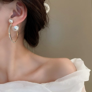 Detail of elegant gold-tone earrings with faux pearls and rhinestones on a female model