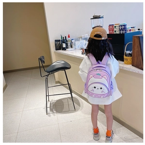 Rear view of a young girl wearing a purple cartoon cat backpack in a cozy indoor setting