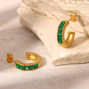 Detailed macro shot of vintage gold C-shape hoop earrings with green zircon inlays