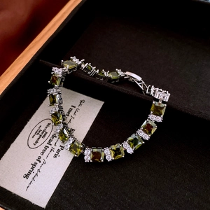 Detail shot of silver tennis bracelet with square olive green and white zircons