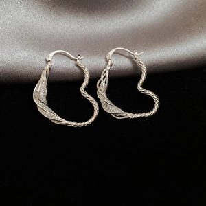Detailed close-up of silver woven heart-shaped hoop earrings on elegant silk background