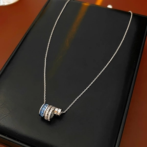 Detailed shot of silver cylinder pendant with blue and white gems and Love Is engraving