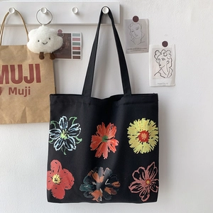 Detail of a black canvas tote bag featuring vibrant hand-painted floral prints and dual straps