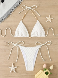 Sexy white two-piece bikini with popcorn texture and shell beads on a wooden background