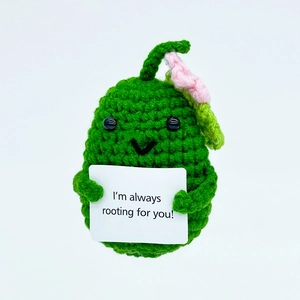 Detail of hand-knitted green avocado toy holding an 'I'm always rooting for you' card